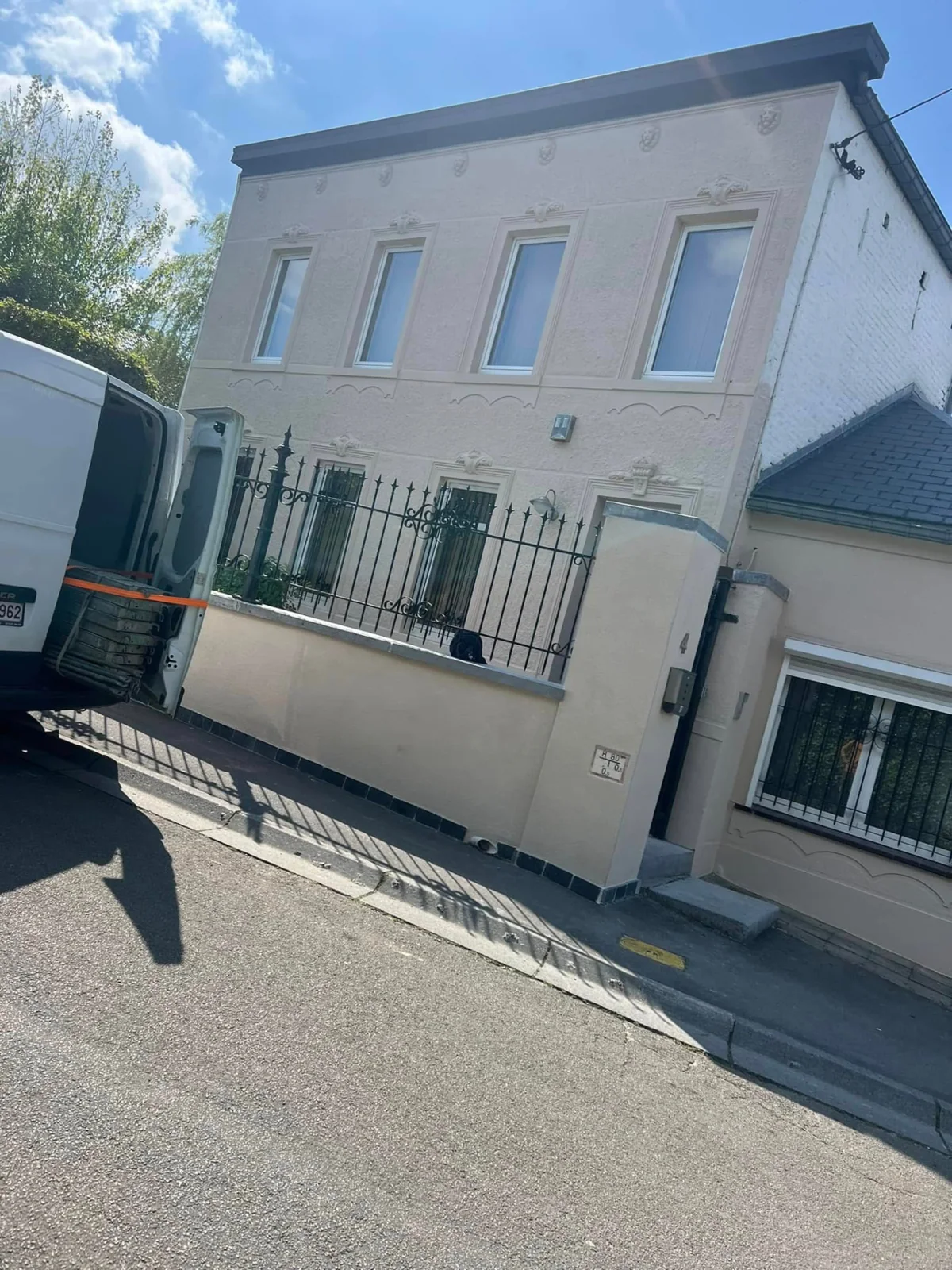 Vue extérieure d’une maison à façade crépie claire, avec clôture au premier plan.
