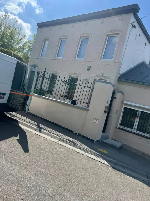Vue extérieure d’une maison à façade crépie claire, avec clôture au premier plan.
