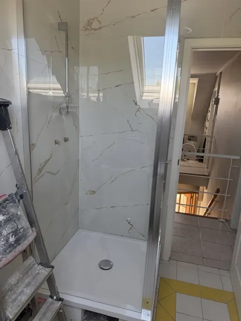 Douche vitrée avec carrelage mural effet marbre, matériel de chantier visible au premier plan.